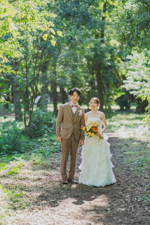 Couple standing hand in hand on a forest path with dappled light, the bride holding a yellow bouquet, a natural pre-wedding photo in a wedding dress
