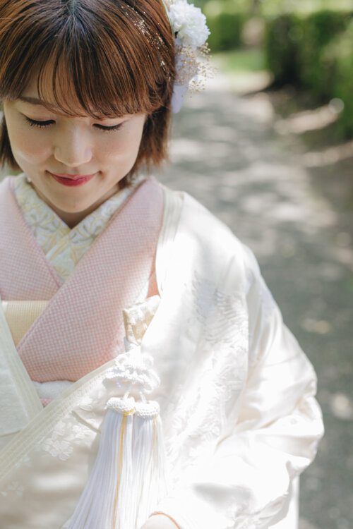 Close-up of a bride in shiromuku with a white flower hair ornament, pink collar and tassel, a detail shot from kimono wedding photos in Japan