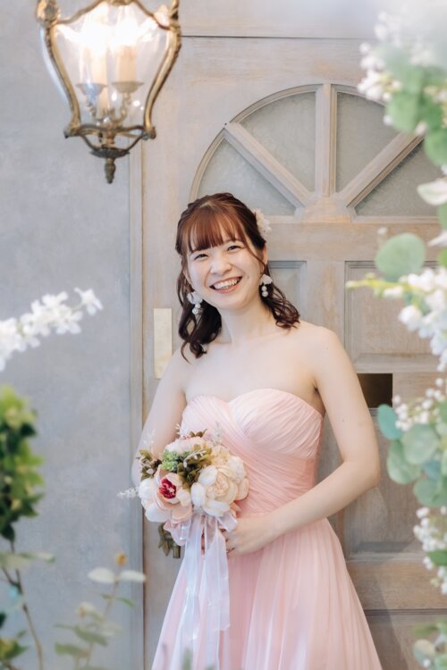 Smiling bride in a light pink strapless tulle color dress holding a bouquet in front of a wooden door and antique lamp, a studio pre-wedding photoshoot in Japan (Light Pink / OCS202)