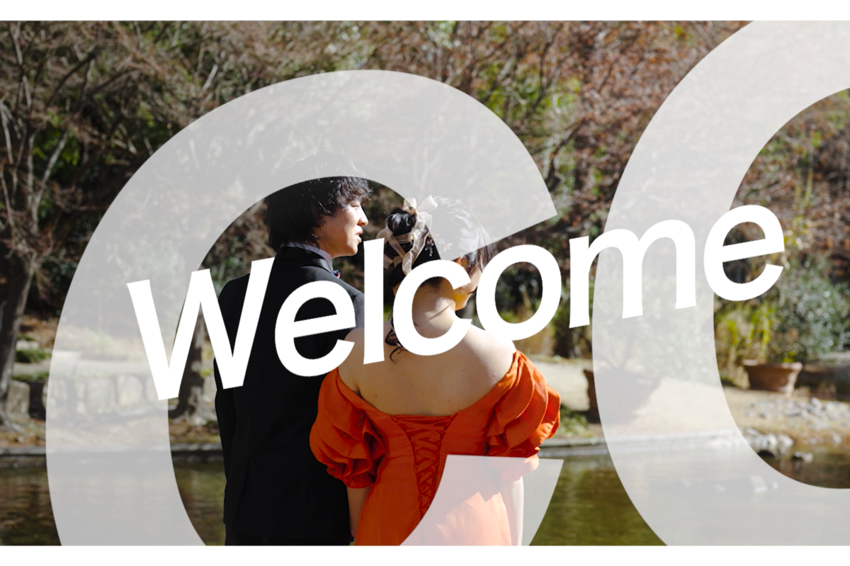 Video still reading 'Welcome', couple in an orange gown and black suit standing together beside a garden pond.