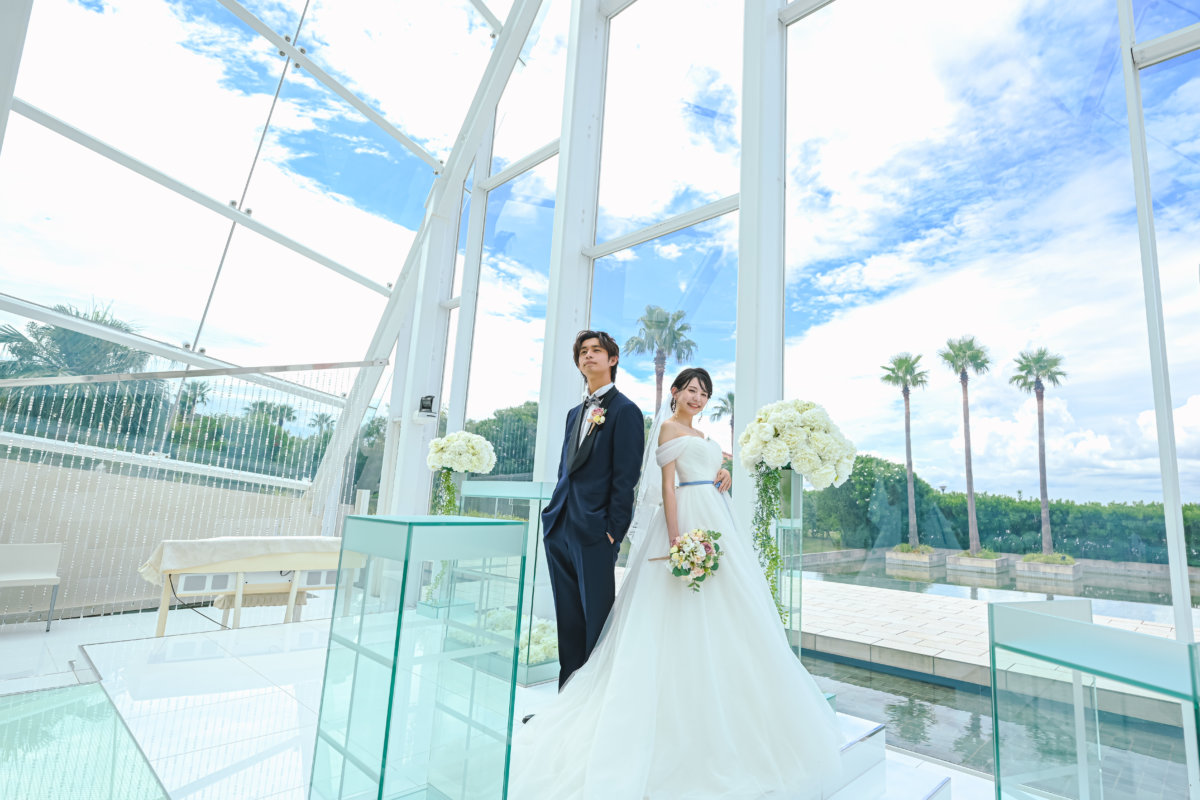 Couple in a wedding dress and tuxedo in a glass chapel overlooking palm trees and blue sky, bright chapel wedding photography