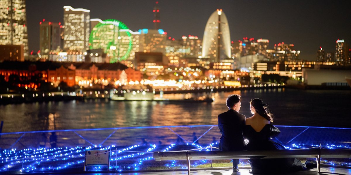 Couple sitting together at night gazing at Yokohama's illuminated skyline and Ferris wheel from Osanbashi Pier.