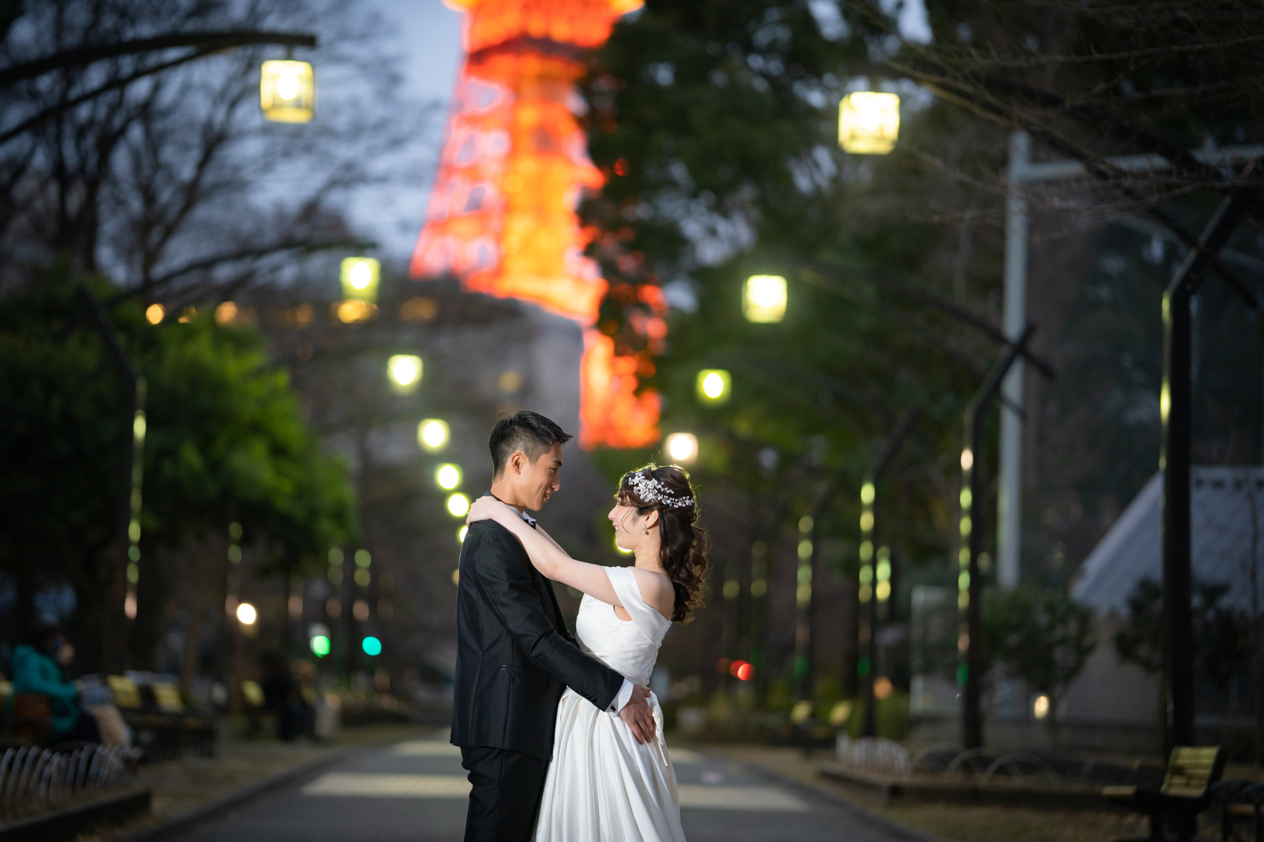 Dancing together beneath a canopy of string lights, Tokyo Tower glowing brightly in the night sky.
