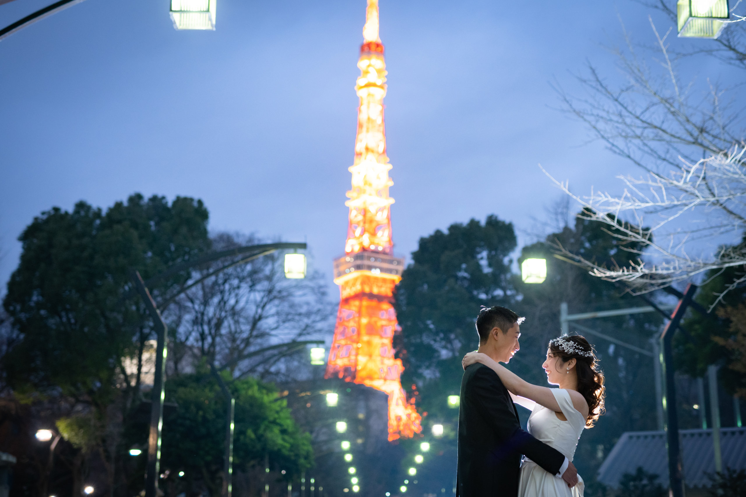 An intimate embrace beneath the glowing red-and-white silhouette of Tokyo Tower at dusk.