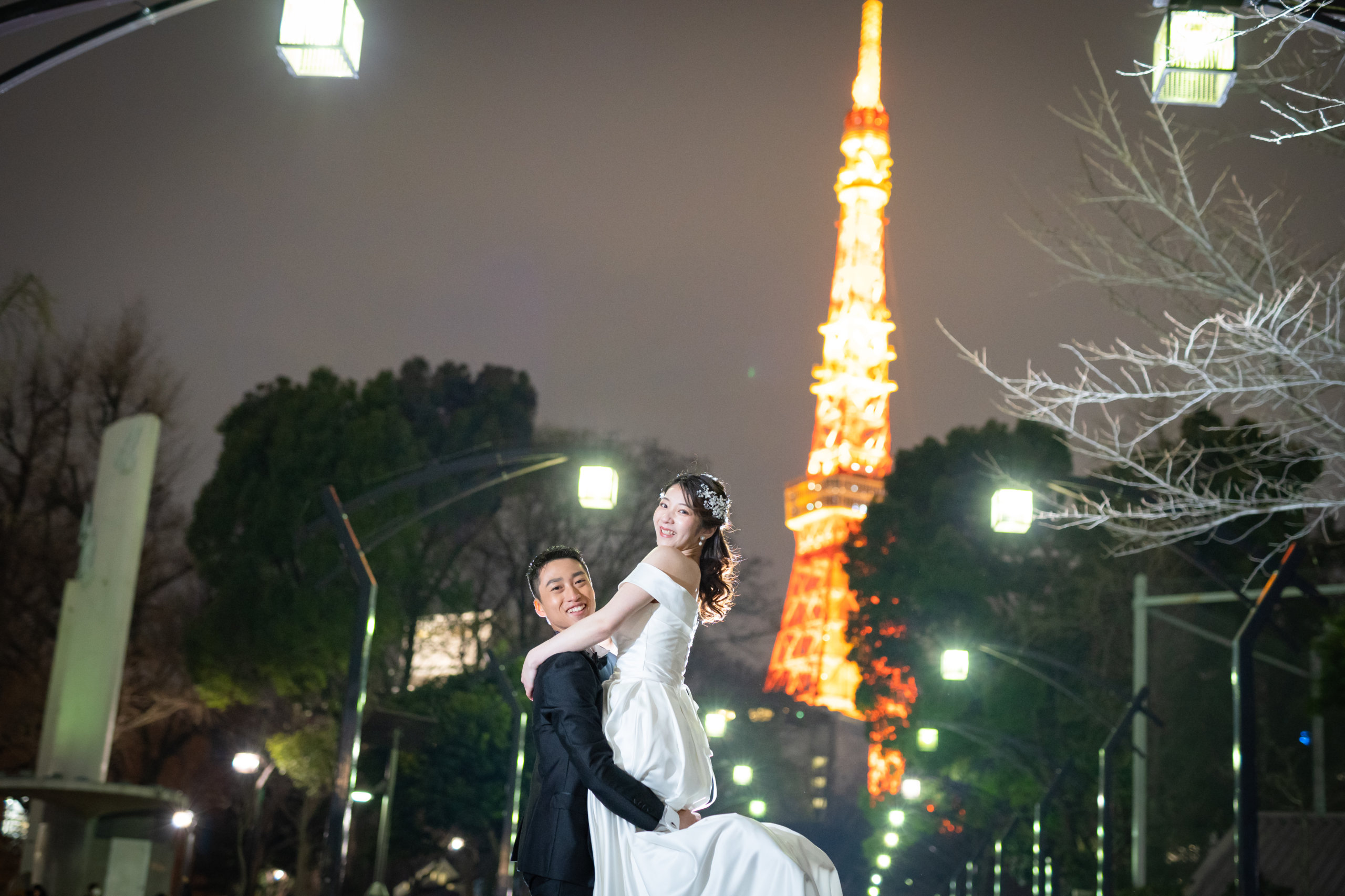 All laughter as the groom lifts his bride off her feet, Tokyo Tower lit up in the background.