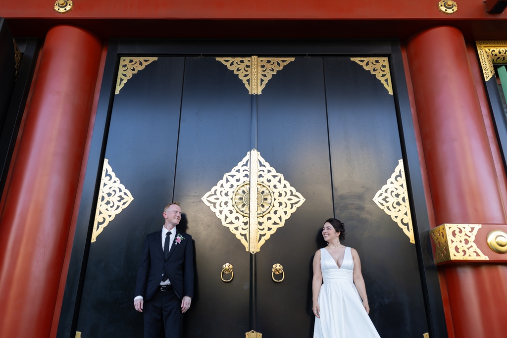 Standing before an ornately lacquered red and gold temple gate, a striking contrast of color and tradition.