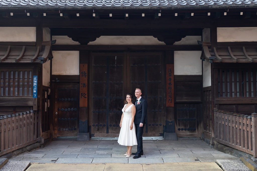The newlyweds pose in front of Senso-ji Temple's historic wooden gate in Asakusa, its weathered doors steeped in centuries of history.