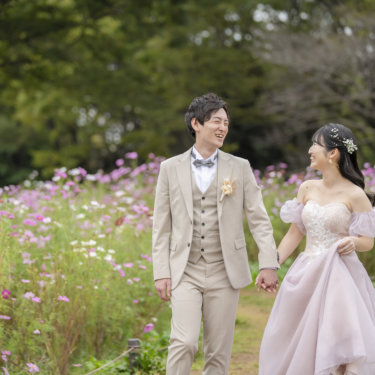 Groom in a beige three-piece suit and bride in a lavender puff-sleeve gown walking hand in hand through a cosmos field in autumn, Japan wedding photography