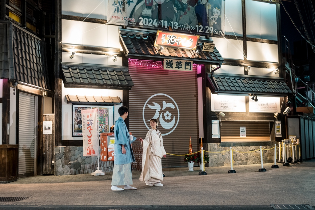 Chatting warmly outside a shuttered shop along Nakamise, Asakusa's famous approach to Senso-ji Temple, lit softly at night.