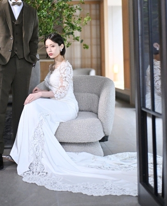 Slender Line style wedding dress (AE01): A sophisticated slender gown featuring delicate lace sleeves and a beautifully figure-hugging silhouette. The soft white hue and elegant, elongated train create a graceful sense of movement, embodying a refined and timeless look for the modern bride.