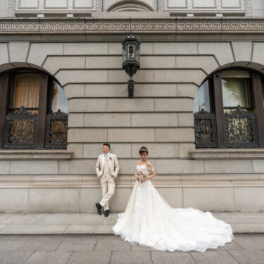Couple posing in front of a symmetrical stone facade with arched iron-grilled windows and a lantern, a classic European-style backdrop for Japan wedding photography in Marunouchi.