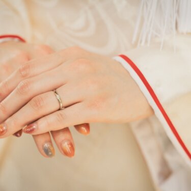 Close-up of a bride's hands resting on her white shiromuku, showing her wedding band and seasonal nail art