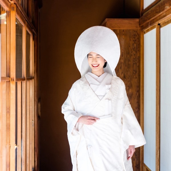 The bride laughs joyfully wearing a traditional white watabōshi hood over her shiromuku kimono.