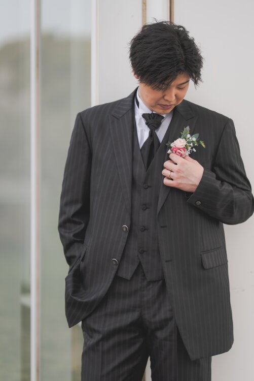 Groom in a black pinstripe tuxedo touching his pink boutonniere, a pre-wedding photoshoot in Japan featuring our larger-size tuxedo (Black Large, TP08).