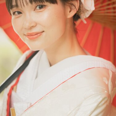 Close-up portrait of a bride in a shiromuku with an orchid hair ornament, framed by the warm red of a Japanese parasol