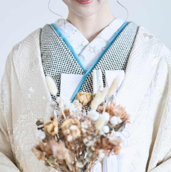A close-up of a bride's kakeshita collar in blue and cream, holding a dried flower bouquet.