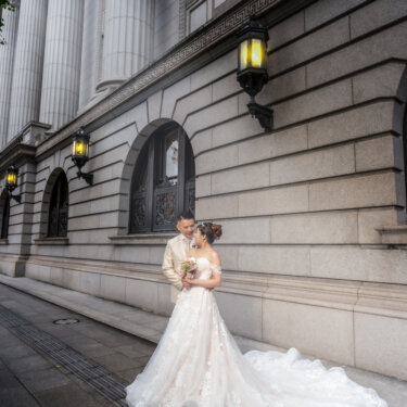 Bride and groom embracing at the foot of a colonnaded stone building with vintage lanterns, her cathedral train pooled on the pavement in this classic wedding photography shot.