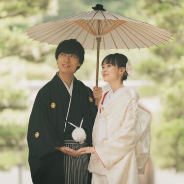 Bride holding a wagasa parasol beside her groom in montsuki, standing among pine trees at a temple from this classic pre-wedding photoshoot in Japan