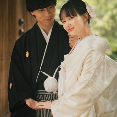 Groom holding a Japanese paper umbrella over his bride in a crane-patterned shiromuku as they hold hands, a pre-wedding photoshoot in Japan