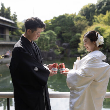 Couple in shiromuku and montsuki toasting beside a garden pond, a relaxed candid from their pre-wedding photoshoot in Japan