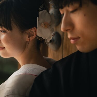 Close-up of a bride in white kimono with an orchid in her hair and her groom in profile beside an old wooden gate