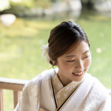 Close-up of a smiling bride in a shiromuku with a floral hair ornament, seated by a garden pond during her Japan wedding photography session