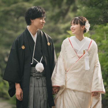 Couple in shiromuku and montsuki with striped hakama walking hand in hand along a leafy garden path from this kimono wedding photos in Japan