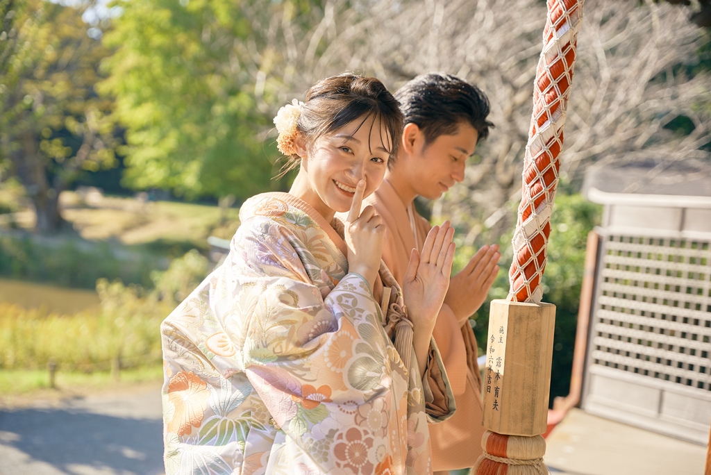 Couple in soft-hued kimono clasping their hands together in prayer at a Shinto shrine, a candid moment from their Japan wedding photography session.