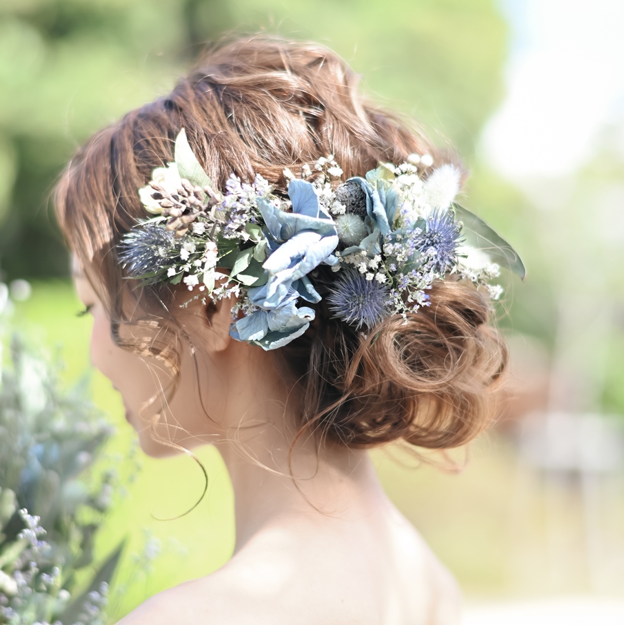 A close-up of a romantic bridal updo accented with blue and white dried flowers, eucalyptus leaves, and thistle blooms.