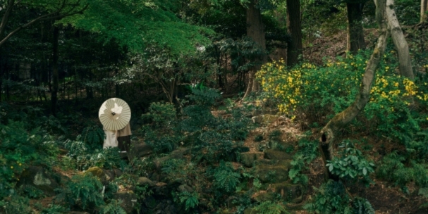 The bride, parasol in hand, walks quietly through a wildflower-dotted woodland at Kansenen Park.