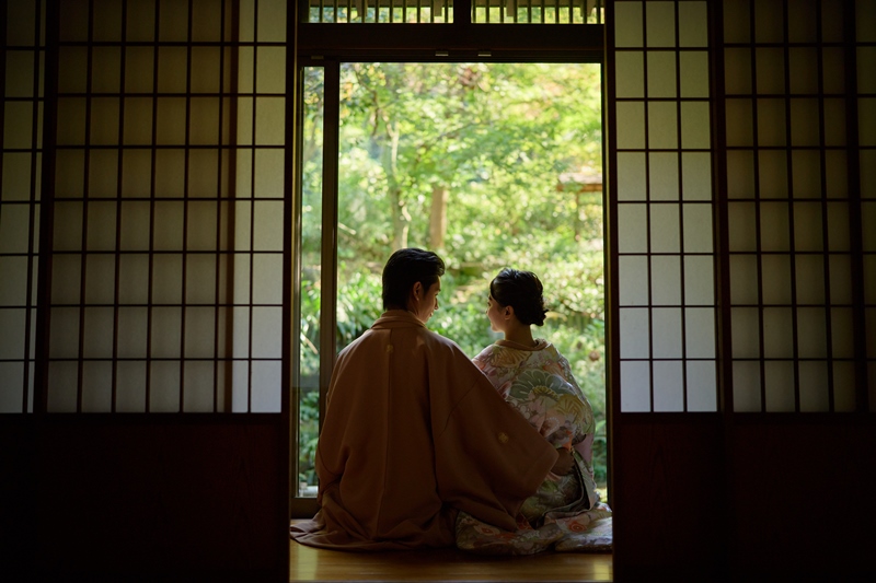 Silhouetted in a doorway, the kimono couple gazes out at a sunlit green garden.