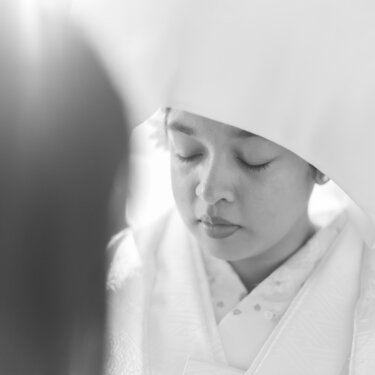 Black-and-white close-up of the bride with eyes closed beneath a white wataboshi hood, a quiet and elegant moment of pre-wedding photography in Japan