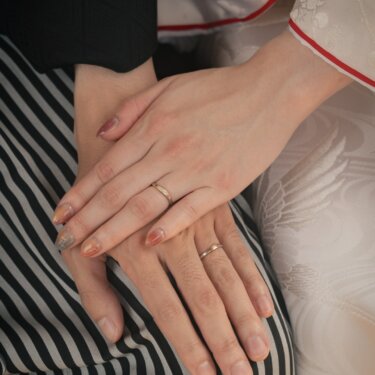 Bride's hand resting on the groom's over his striped hakama, both wearing wedding rings, during a Japanese kimono photoshoot