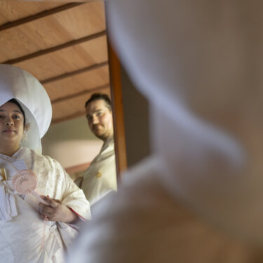 Bride in a white wataboshi and shiromuku framed through a sliding door with the groom behind her, a creative framing idea for wedding photography in Japan