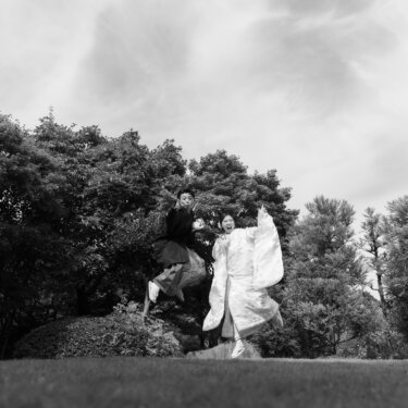Black and white shot of a couple in wedding kimono jumping in the air above a Japanese garden, full of joy and movement
