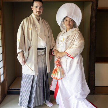 Full-length portrait of the groom in hakama and the bride in a shiromuku with a red-lined train standing on tatami, traditional kimono wedding photos in Yokohama