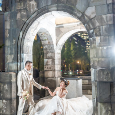 Groom taking the hand of his bride seated on the steps of a lantern-lit stone archway in Marunouchi, her ball gown spreading around her in this evening wedding photoshoot.