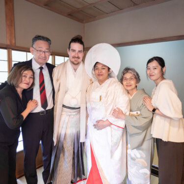 Bride in a white shiromuku and wataboshi hugging her family in a shoji-lit tatami room, a heartwarming family portrait from a Japanese wedding photoshoot