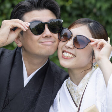 Close-up of a couple in wedding kimono lowering their sunglasses and grinning, a fun candid from their Japan wedding photography session