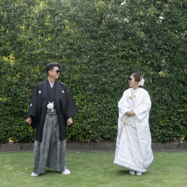 Bride in a white shiromuku and groom in montsuki wearing sunglasses on a lawn, a lighthearted take on kimono wedding photos in Japan