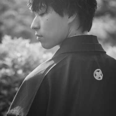 Black-and-white portrait of a groom in montsuki with the family crest on his back, looking down quietly in a Japanese garden