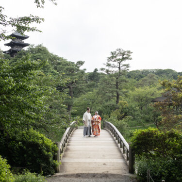 Wide view of Sankeien Garden with the three-story pagoda on the hill and a kimono couple standing on the arched bridge, a classic pre-wedding photoshoot in Yokohama