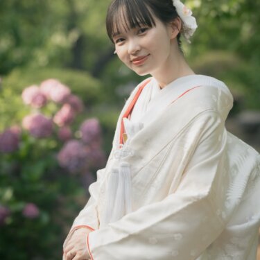 Smiling bride in a crane-patterned shiromuku standing beside pink hydrangeas, a natural pre-wedding photoshoot in Japan