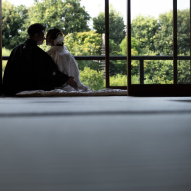 Silhouetted couple in wedding kimono leaning close to each other against bright garden windows, an atmospheric Japan wedding photography shot