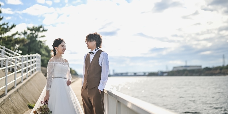 Chatting warmly along the waterfront promenade at Hamadera Park, city rooftops visible across the bay.
