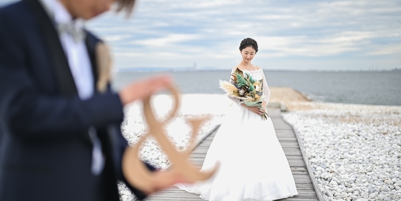 Bride with a bouquet walking along a stone breakwater path beside the ocean at Marble Beach.
