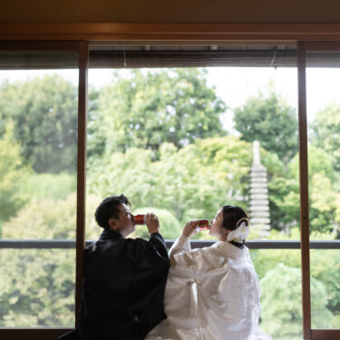 Bride and groom sharing a sake toast on tatami in front of a garden view with a stone pagoda, a San-san-kudo moment from a Japanese wedding photoshoot