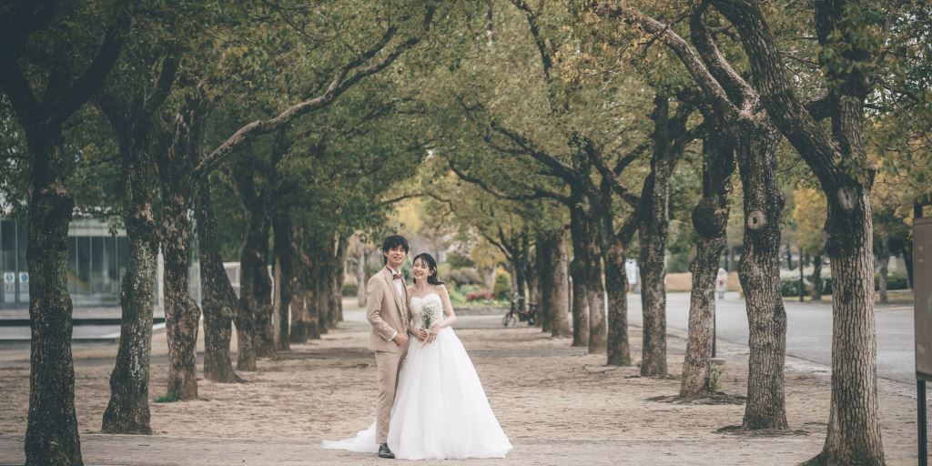 Couple standing beneath a tunnel of leafy trees along a wide tree-lined path at Tsurumi Ryokuchi Park.