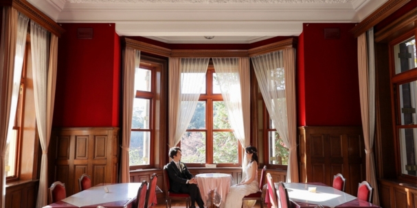 Seated by lace-curtained windows in a deep red drawing room at Kyu-Furukawa Gardens, a refined and intimate portrait.