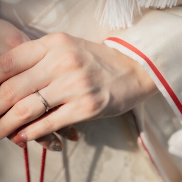 Close-up of a bride's hand with her wedding ring resting on a white shiromuku kimono trimmed in red, from a kimono wedding photoshoot in Japan